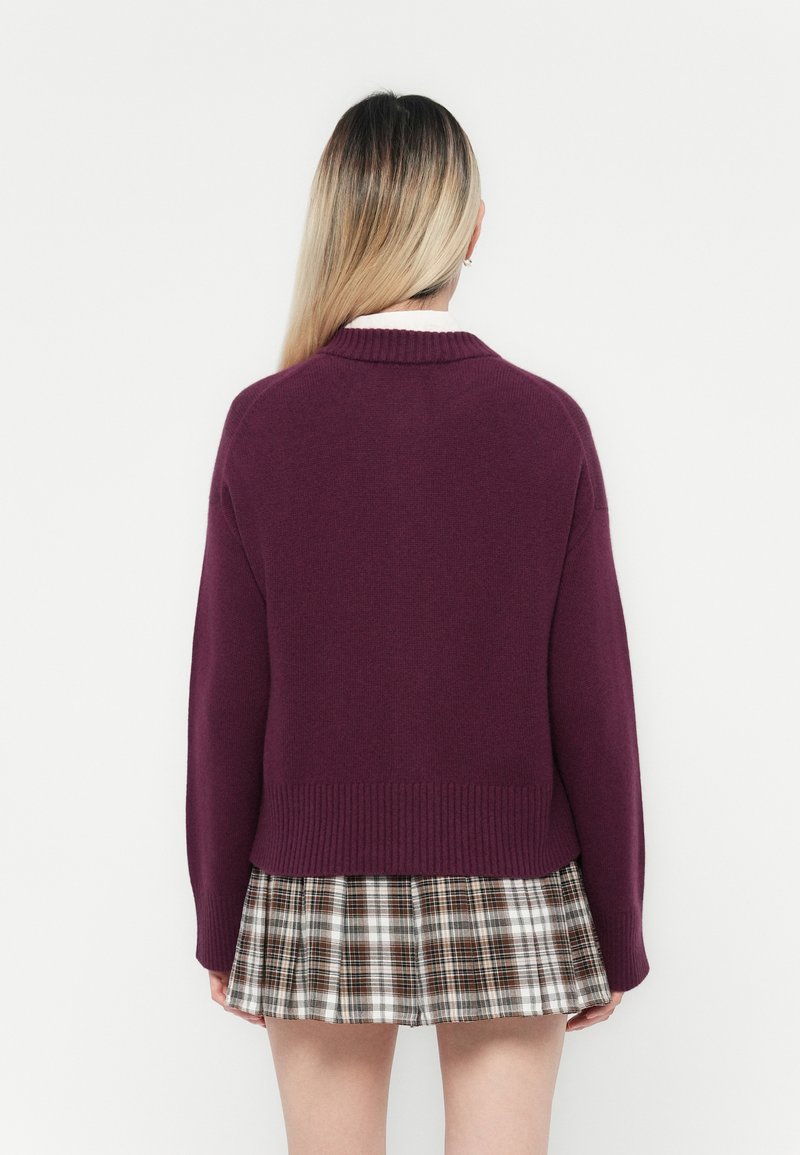 Bordowy sweter z dzianiny z prążkowanym dołem, zestawiony z plisowaną spódnicą w kratkę w brązowe, białe i szare wzory.