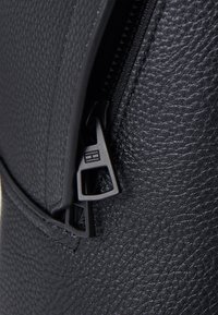 Bolso de cuero negro texturizado que presenta una cremallera suave con una tira de tira geométrica audaz. Una costura detallada acentúa la estructura.