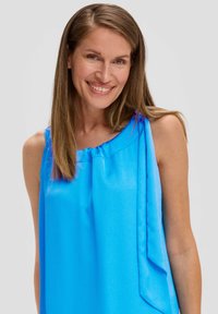 Helles blaues ärmelloses Top aus strukturiertem Stoff, mit gerafftem Ausschnitt und asymmetrischem Design mit seitlichem Drapé.