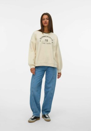 Sweatshirt crème avec le texte vert "SUMMERVILLE 78 Caroline du Sud", associé à un jean large bleu clair et des baskets noir et gris.