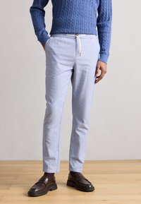 Ανοικτό μπλε, ραμμένα στα μέτρα παντελόνια από απαλό ύφασμα με ελαστική μέση με κορδόνι, εμπρόσθιες τσέπες και σχεδιασμό με στενή γάμπα. Το look ολοκληρώνουν καφέ μοκασίνια.