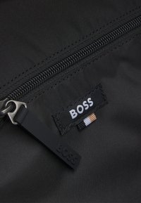 Black fabric zip pocket with a silver zipper, featuring a stitched "BOSS" label and a textured black zipper pull.