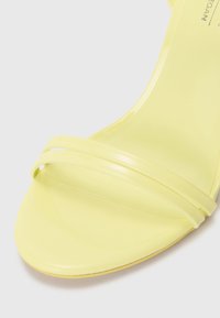 Sandal con tacco trasparente giallo, caratterizzata da due sottili cinturini sulla parte anteriore, texture liscia e design minimalista.