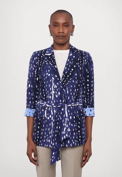 Blazer bleu marine avec motif éclaboussé blanc, accents de poignet bleu clair, ceinture à nouer à la taille, manches trois-quarts, texture lisse.