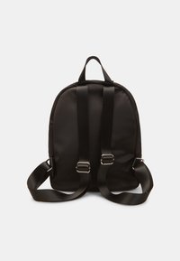 Mochila de tela negra con diseño acolchado, correas ajustables dobles y asa superior. Presenta herrajes metálicos y una textura suave.