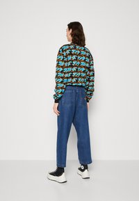 Sweatshirt preto com padrão de ondas azuis e laranjas, emparelhado com jeans de denim azul de corte largo. Ténis pretos com solas brancas.