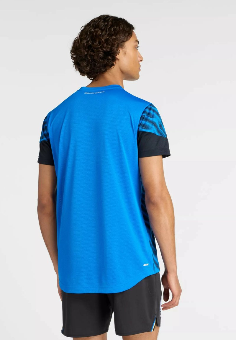 Maglietta sportiva blu con dettagli neri, maniche corte, schiena texturizzata e orlo arrotondato; abbinata a pantaloncini neri.