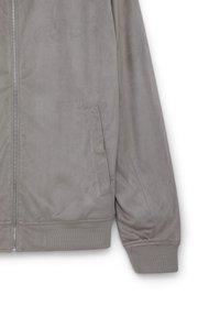 Giacca bomber grigia realizzata in un giovane materiale morbido simile al suede. Presenta una zip frontale, polsini a coste e tasche laterali. Design semplice e testurizzato.