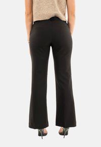 Pantalones acampanados negros con una textura suave y un corte ajustado. Cuenta con pasadores para cinturón y bolsillos, combinados con zapatos de tacón alto.