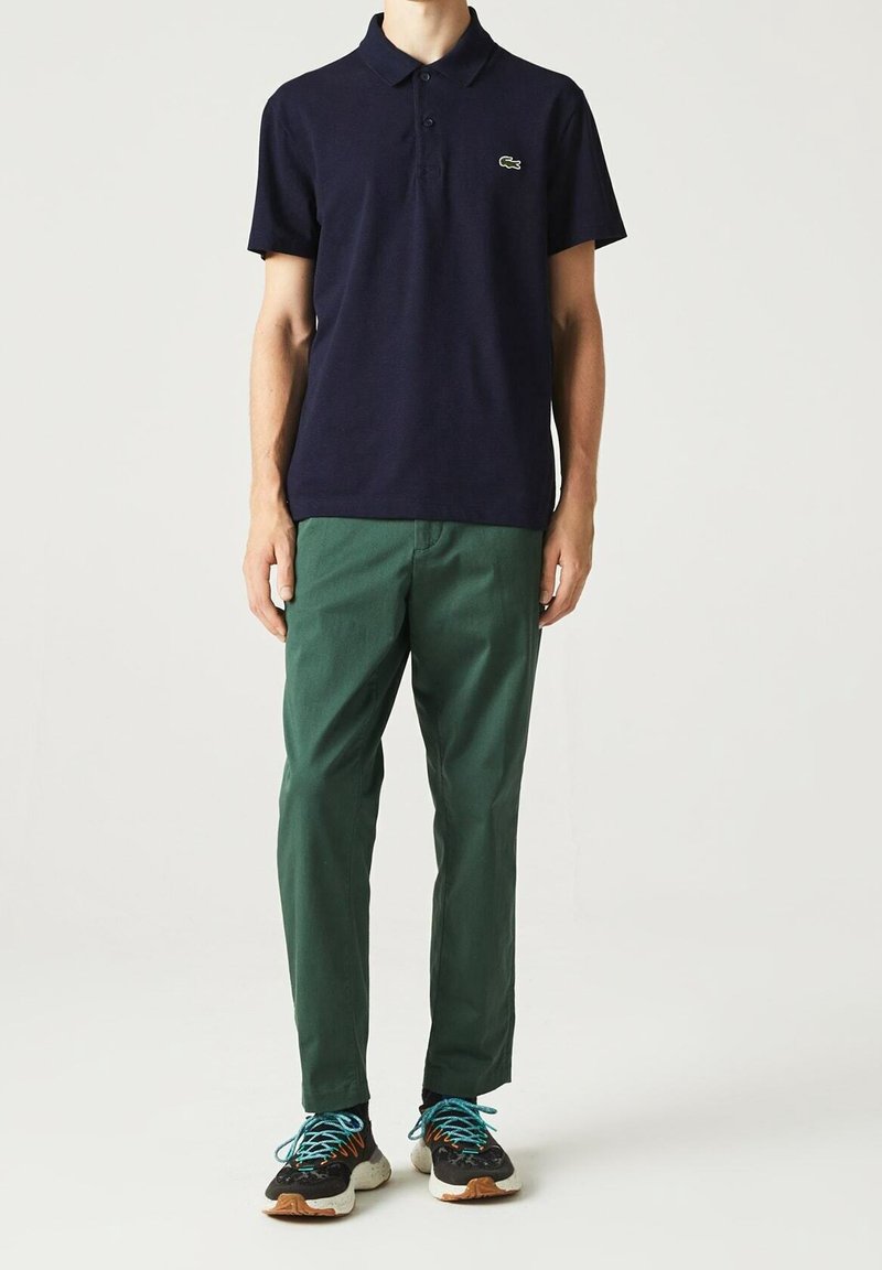 Polo-shirt marine avec un logo vert, associé à un pantalon vert et des baskets multicolores avec des accents noirs, blancs et oranges.