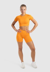 Oranje sportieve crop top en bijpassende hoge shorts, gemaakt van een soepele, rekbare stof, met een slim fit ontwerp en korte mouwen.