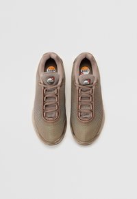 Sport shoes in brown mesh with a textured design. Features light green accents, round logo, and lace-up closure. Round toe with a cushioned sole.