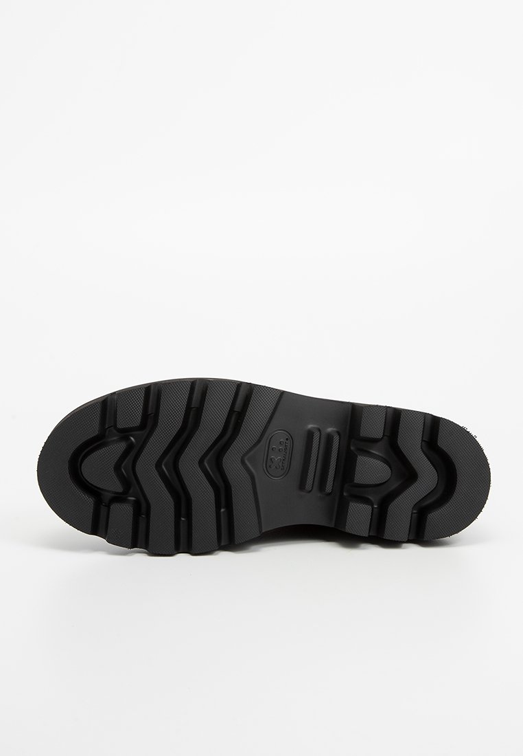 Semelle de chaussure en caoutchouc noir avec des motifs de crampons profonds, comportant plusieurs rainures et une surface texturée pour une meilleure adhérence. Logo clair embossé au centre.