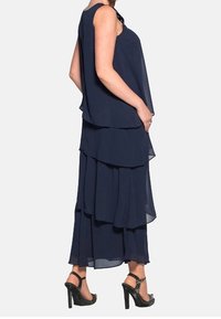 Navy blue layered dress with a flowing design, featuring a scoop neckline and sheer fabric. Paired with black strappy high-heeled shoes.