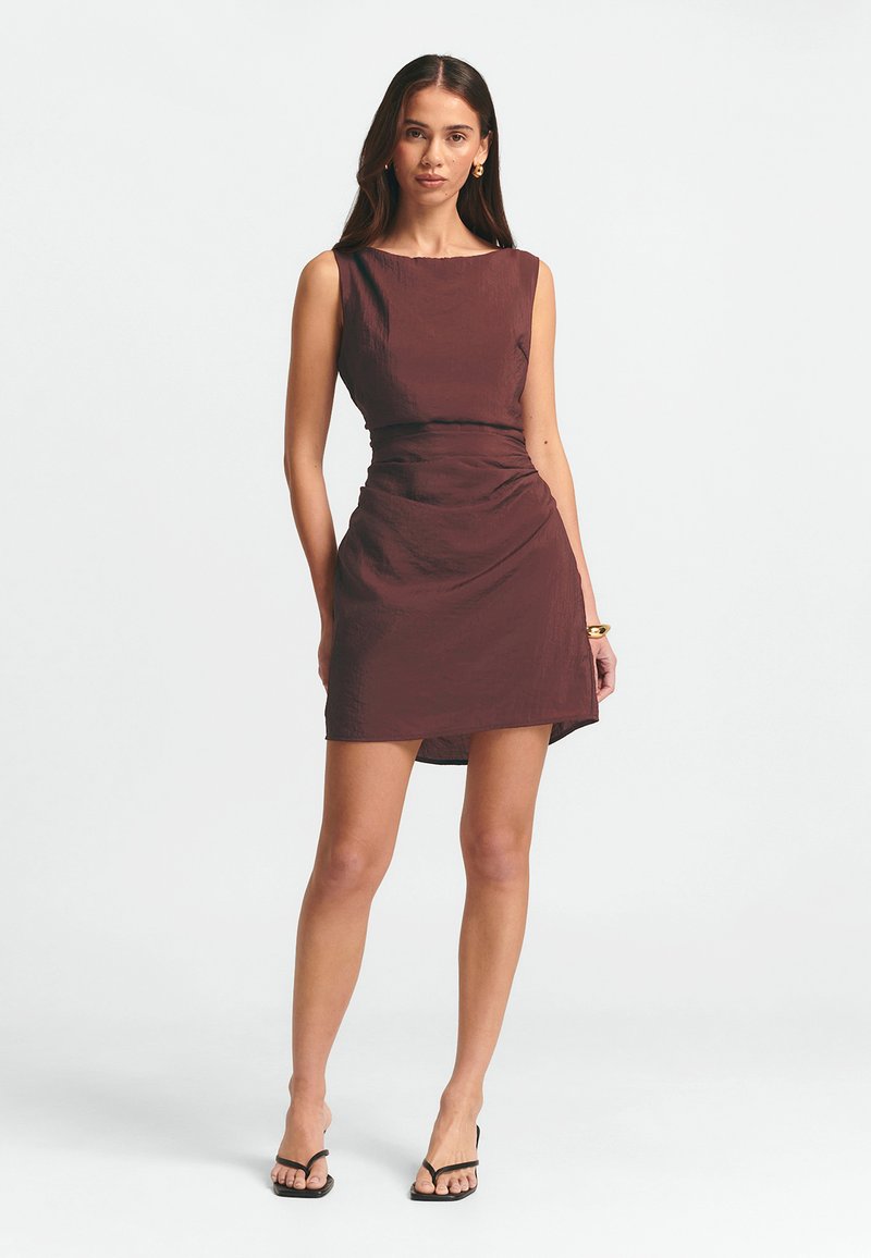 Prigludusi be rankovių suknelė tamsiai burgundiško atspalvio, su raukšlėta juosmens dalimi ir sijonu, kuris siekia virš kelių. Dėvima su juodais sandalu.