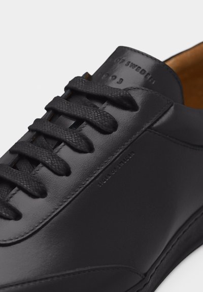 Μαύρο δερμάτινο αθλητικό παπούτσι με υφασμένες μαύρες κορδόνια, ανάγλυφο λογότυπο στη πλευρά και ταμπά εσωτερική επένδυση.