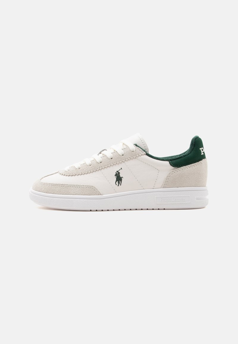 Baskets basses blanches avec des accents en suède beige, languette de talon verte, lacets blancs et un logo noir de joueur de polo sur le côté.