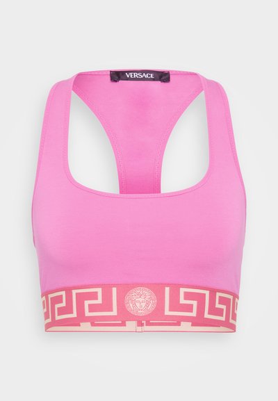 Roza športna modrc z zasnovo v racerback slogu. Ima kontrastni bež trak z grškim vzorcem in medaljon na sredini.