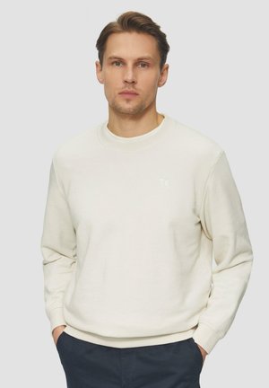 Sudadera de cuello redondo en color beige claro, mezcla de algodón, puños y dobladillo acanalados, con un branding mínimo en el pecho, corte relajado y textura suave.