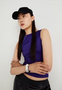 Haut ajusté sans manches violet avec un col rond, associé à un pantalon en cuir noir ; accessoirisé avec un bracelet en argent et une casquette noire.
