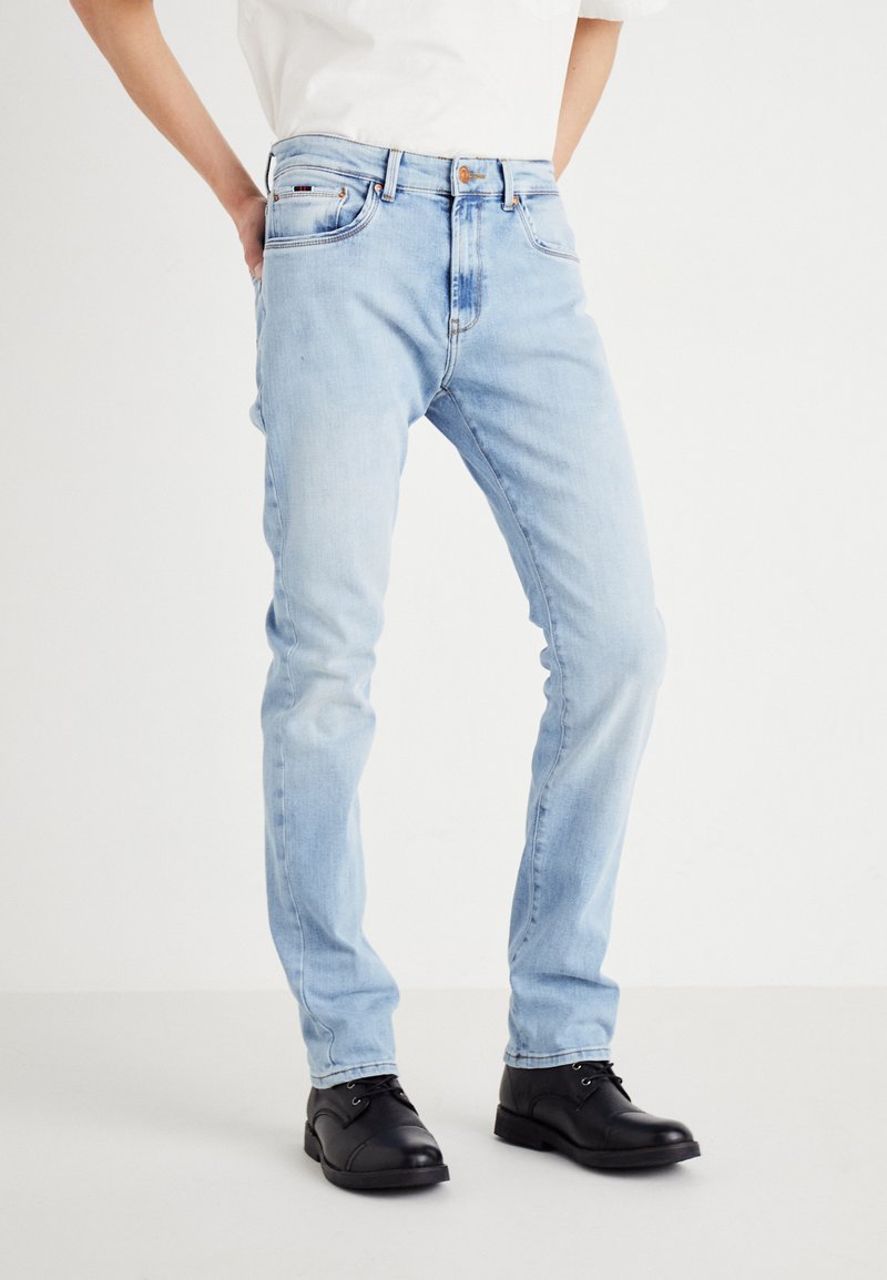 Jeans de mezclilla azul claro con corte ajustado, que cuentan con cinco bolsillos, un cierre frontal con botón y detalles de desgaste sutiles.