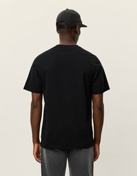 Čierne tričko s krátkym rukávom, z bavlnenej látky, klasický strih. Sivé nohavice, štruktúrovaný materiál. Čierna čiapka s vzorom houndstooth.