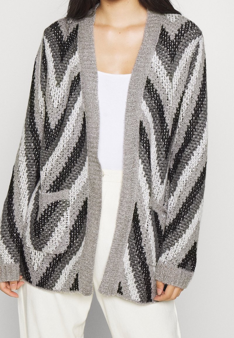 Cardigan à motifs gris et noirs avec ouverture devant, manches longues et poches latérales. Confectionné en tissu tricoté texturé.
