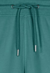 Ceinture à cordon de serrage bleu sarcelle avec embouts métalliques passés dans des œillets métalliques sur le tissu côtelé du haut du vêtement bleu sarcelle.