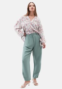 Blusa floreale con sfondo bianco, maniche lunghe e scollatura a V abbinata a pantaloni verdi menta a vita alta con dettagli a bottoni.