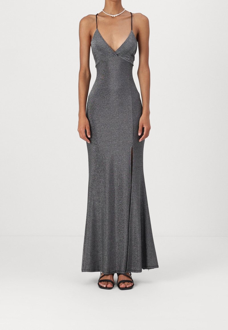 Robe de soirée argentée ajustée sans manches avec fines bretelles, décolleté en V, fente devant, associée à des sandales noires à bout ouvert et un collier de perles.