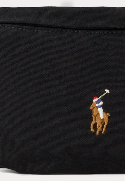 Czarna tkanina z małym wyhaftowanym jeźdźcem polo w czerwonej czapce i niebiesko-białym ubraniu na brązowym koniu.