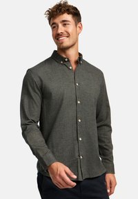 Chemise boutonnée vert foncé en tissu texturé, avec un col, des manches longues et des boutons de couleur claire.