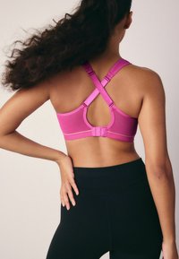 Felroze sportbeha met een hoge rug, gekruiste banden, mesh panelen en verstelbare sluitingen. Gecombineerd met zwarte hoge taille legging.