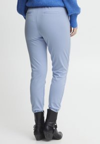 Hellblaue, schmal zulaufende Hosen mit glatter Textur und Gesäßtaschen, kombiniert mit schwarzen Ankle Boots mit dekorativen Riemen und strukturierten Akzenten.