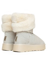 Botas de ante beige claro con un puño de piel de piel sintética cremosa y una suela de goma beige; presenta un pequeño logo en el talón trasero.