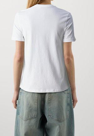 Camiseta blanca de algodón con mangas cortas y un escote redondeado, combinada con pantalones cortos de mezclilla azul claro de corte oversize que cuentan con grandes bolsillos traseros.