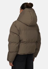 Giacca puffa marrone con un ampio cappuccio, caratterizzata da una forma squadrata e una texture trapuntata. La giacca ha polsini elasticizzati e un design corto.