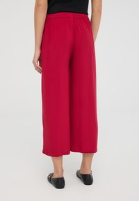 Pantaloni larghi rossi con vita elastica, realizzati in un tessuto morbido e leggero, di lunghezza cropped, abbinati a scarpe nere basse.