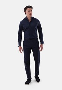 Dunkelblaues Hemd mit leicht strukturiertem Kragen, kombiniert mit marinefarbigen Hosen und dunklen Schuhen. Der Stoff hat eine dezente Textur und ist tailliert geschnitten.