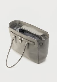 Bolso tote de cuero gris con una forma estructurada, que cuenta con un bolsillo exterior, herrajes plateados y cierre seguro con cremallera. El interior es de color gris claro.