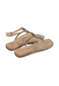 Sandalias de ante beige con piedras turquesas decorativas en la correa, suela plana y correa ajustable en el tobillo. Etiquetadas "ALMA EN PENA."