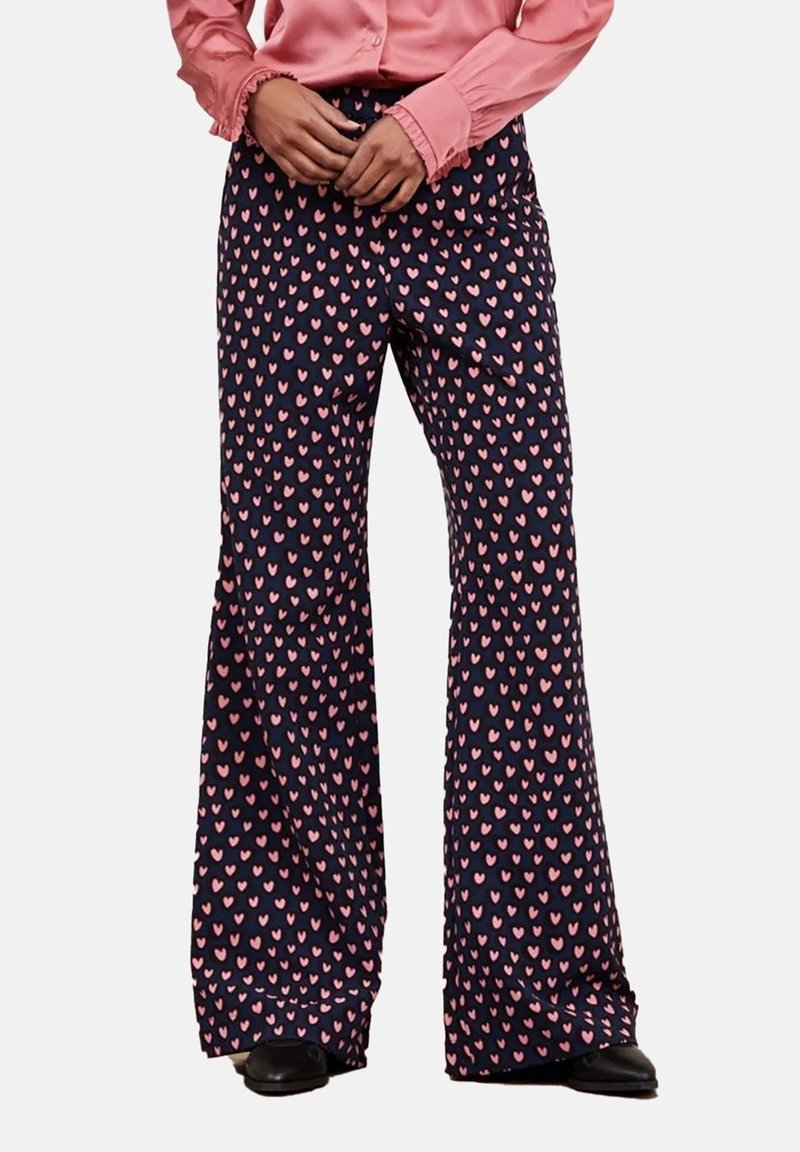 Marinblå byxor med ett upprepat mönster av rosa hjärtan, utsvängd design, mjukt tyg och avslappnad passform, kombinerat med en ljusrosa blus.