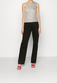 Silver sequin one-shoulder top paired with black straight-leg jeans and pink heeled sandals, showcasing a fitted silhouette and shimmering texture.
