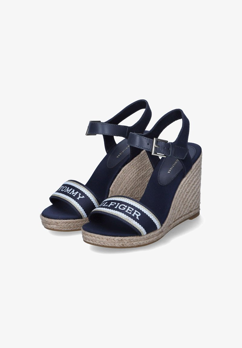 Marinefarbene Wedge-Sandalen mit einer gewebten Jutesohle, ausgestattet mit zwei breiten Riemen. Ein Riemen ist mit dem weißen Text "TOMMY HILFIGER" in glatter Textur versehen.