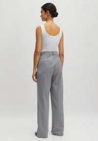 Graue weit geschnittene Hose aus strukturiertem Stoff, mit zwei Gesäßtaschen und hoher Taille. Das Outfit wird mit einem weißen Tanktop abgerundet.