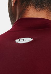 Mørkerød sportsærme med et glat, tekstureret stof. Har et rundt logo mærke på nakken bagtil til identifikation af mærket.