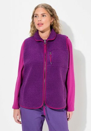 Gilet en polaire violet avec une fermeture éclair à l'avant, un col montant et une poche poitrine. Associé à un haut à manches longues rose et un pantalon violet.