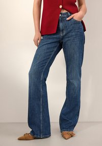 Jeans a zampa d'elefante blu scuro in denim, con vita media, design classico a cinque tasche, con cuciture a contrasto discrete e una finitura pulita.