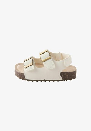 Hvid sandal lavet af syntetisk materiale med to justerbare remme, guldfarvede spænder og en tekstureret brun sål.