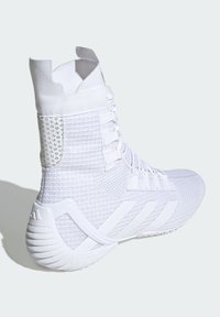 Zapatilla deportiva blanca con parte superior texturizada, sección de malla con patrón y tres franjas blancas en el costado. Diseño de cuello tipo calcetín.